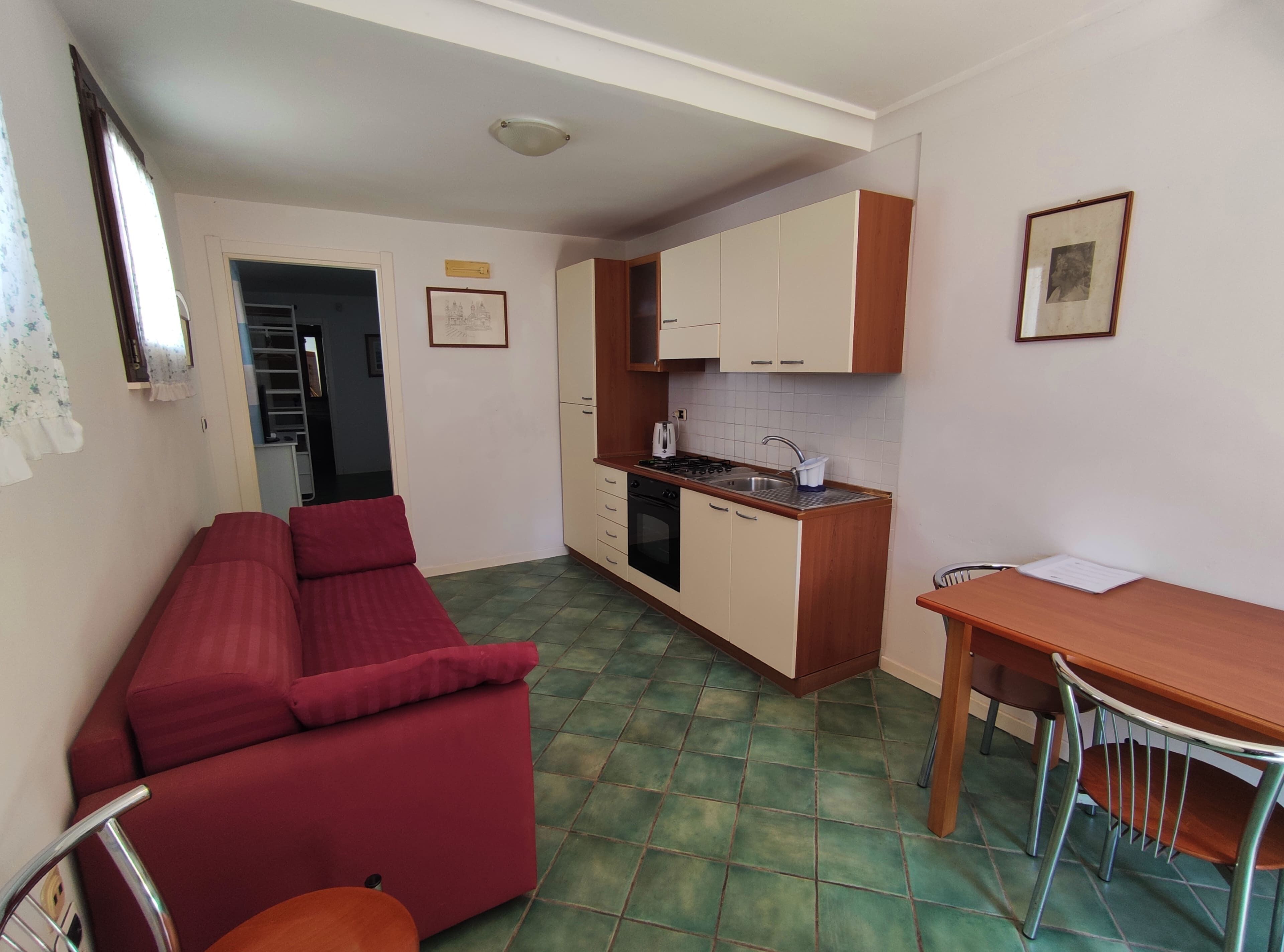 A compact living space with a kitchenette, a dining area, and a red sofa.