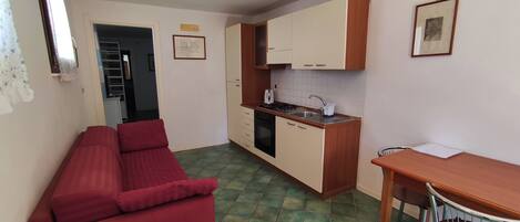 A compact living space with a kitchenette, a dining area, and a red sofa.