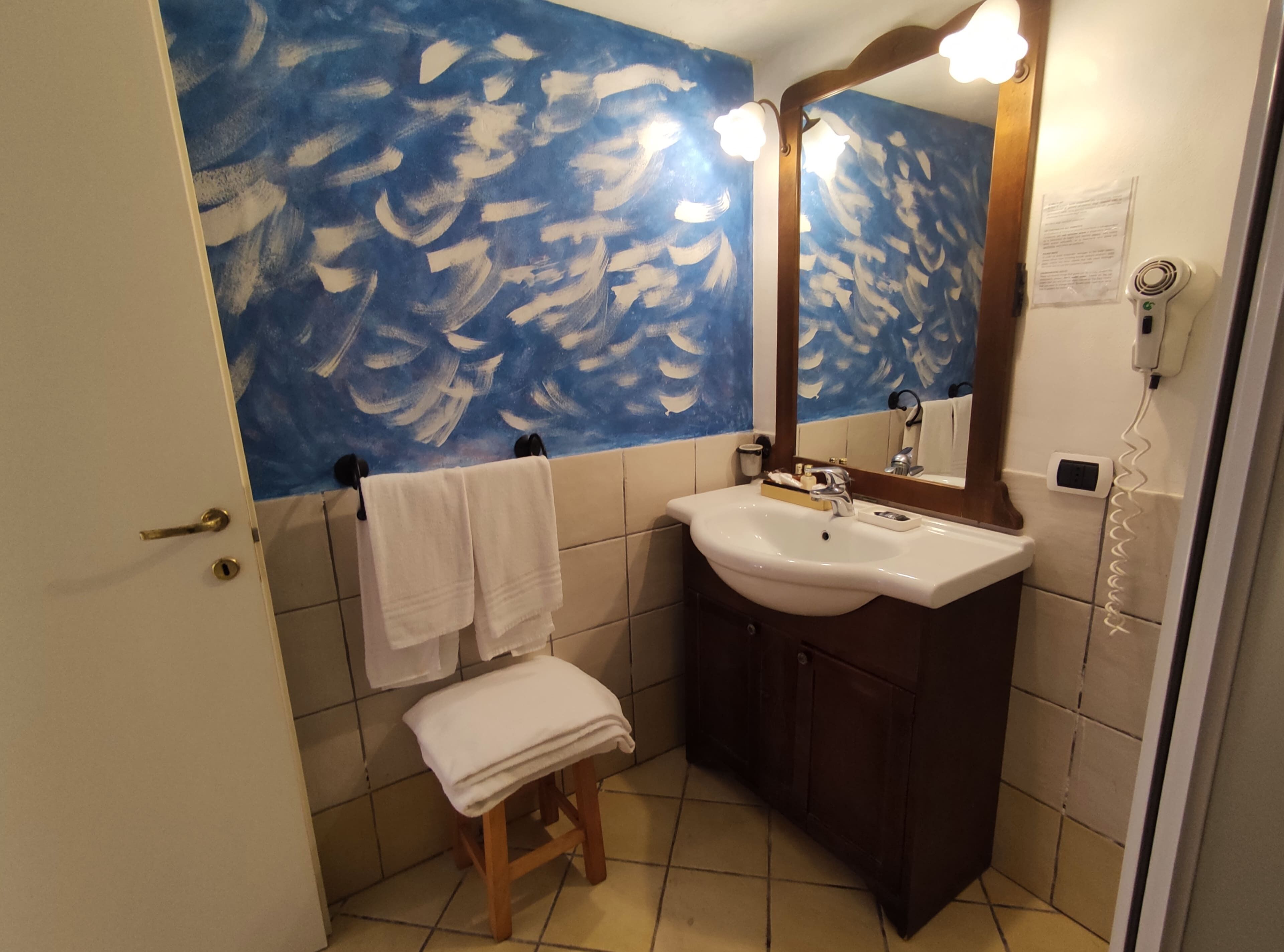 A bathroom with a blue wall, white tiles, a sink, a mirror, a towel rack, and a small stool.