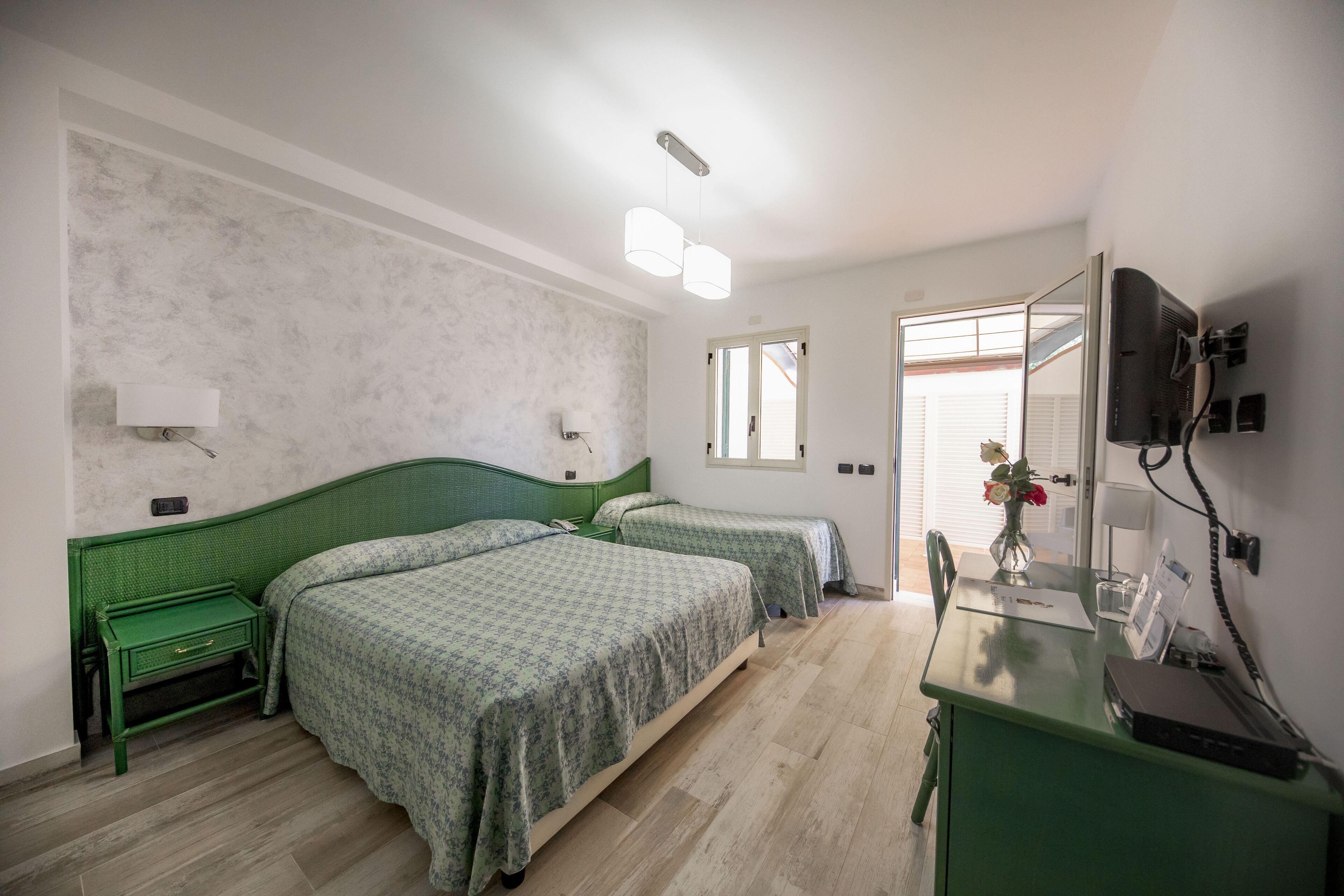 A bedroom with two beds, a desk, a mirror, and a TV.