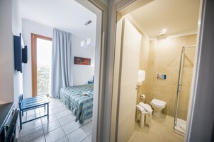 Una habitación de hotel con cama, sillón, escritorio, ducha y váter.
