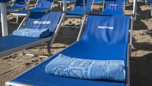 Een rij blauwe ligbedden met handdoeken erop, gelabeld 'BAJA DEL CAPITANO'.