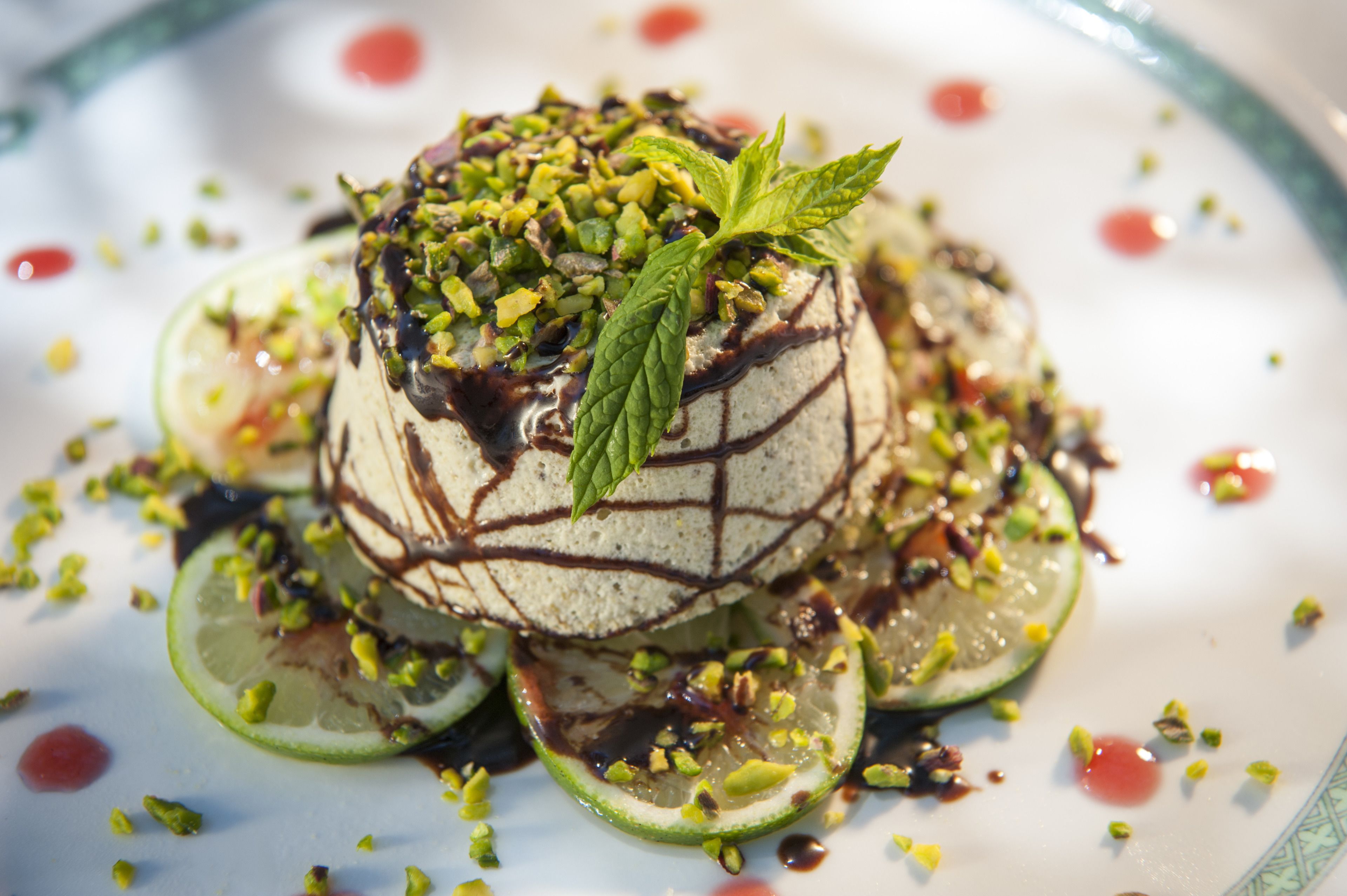 A dessert with a mint leaf garnish, surrounded by lime slices and chopped pistachios.