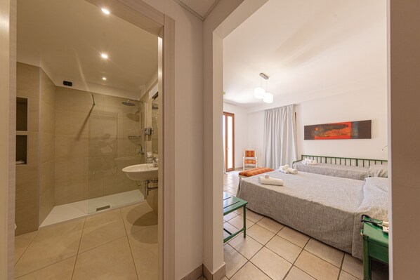 Una habitación de hotel moderna con ducha, lavamanos, cama y una mesita.