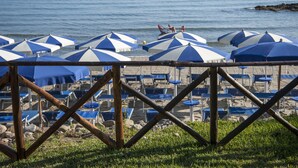 Een strand met rijen blauw-wit gestreepte parasols en ligstoelen.