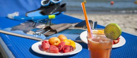 Una mesa en la playa con una bebida, fruta y un par de gafas de sol.