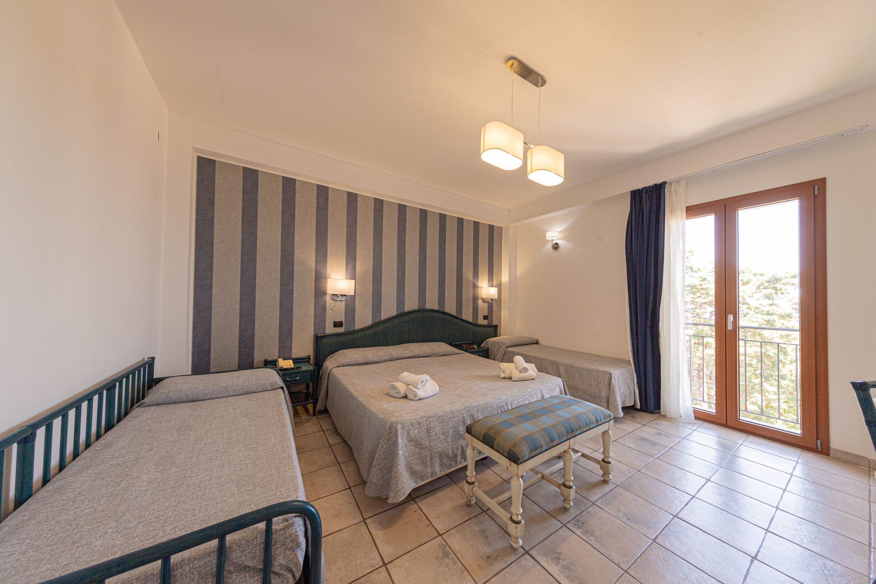 Une chambre d’hôtel avec deux lits, un banc, un balcon et un mur à rayures.