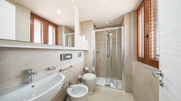 A modern bathroom with a sink, bidet, toilet, and glass-enclosed shower.