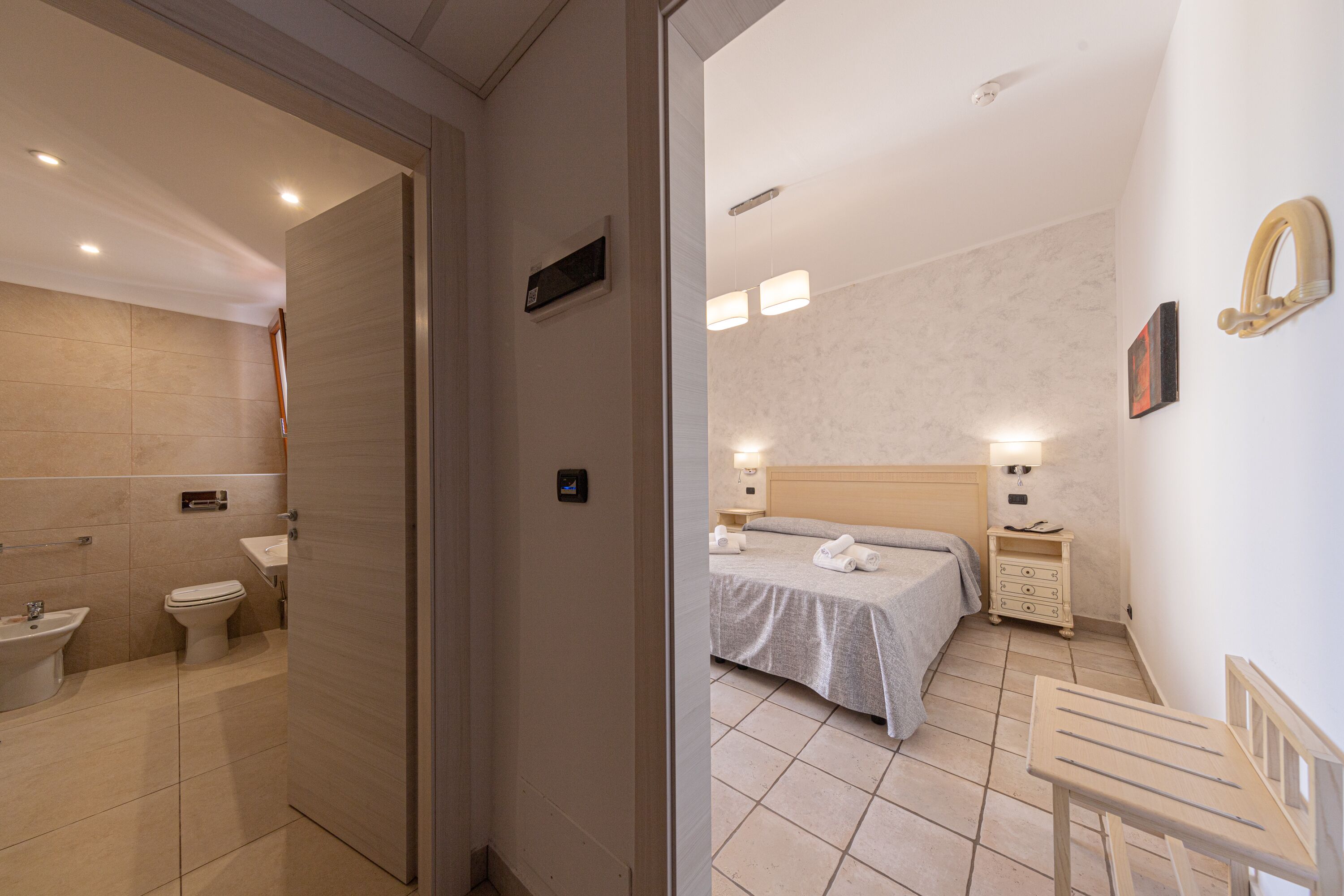 Una habitación de hotel con baño, cama, mesita de noche y velador.