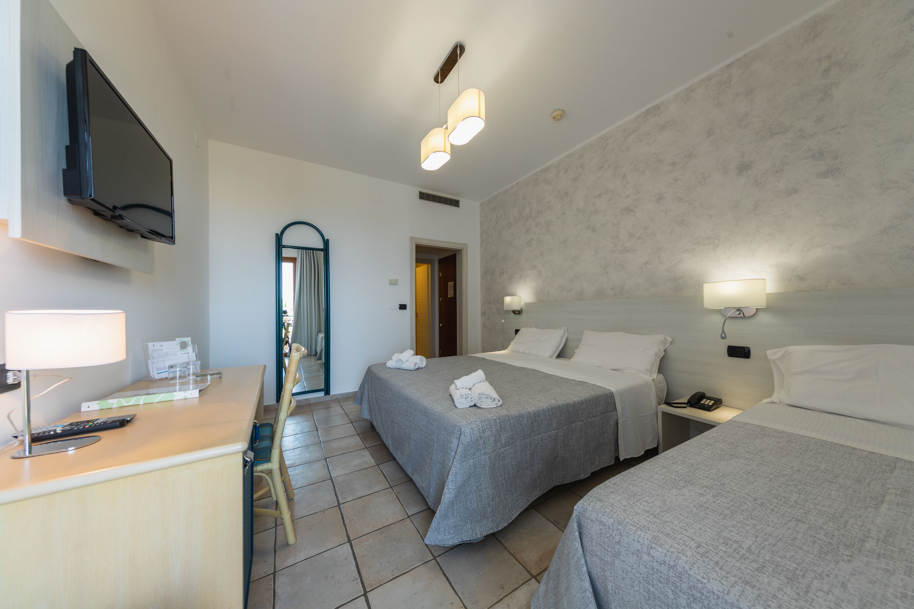 A hotel room with two beds, a desk with a lamp, a TV, and a bathroom door.
