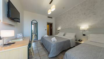 A hotel room with two beds, a desk with a lamp, a TV, and a bathroom door.