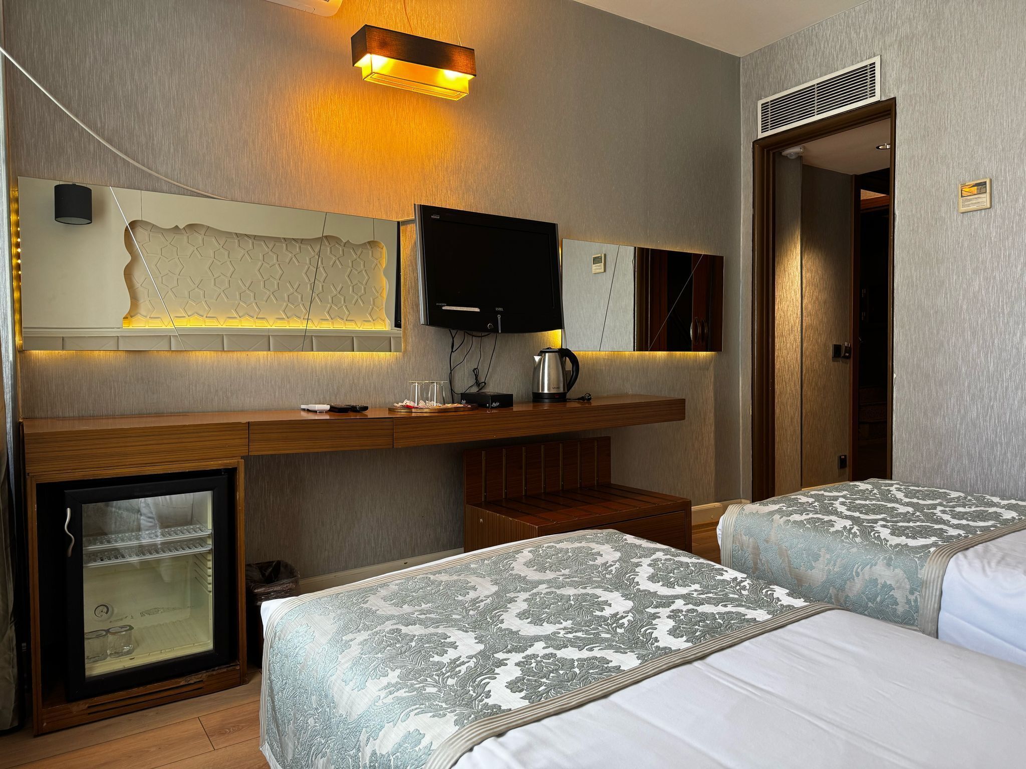 A hotel room with a bed, bedside tables, a television, a minibar, and a refrigerator.