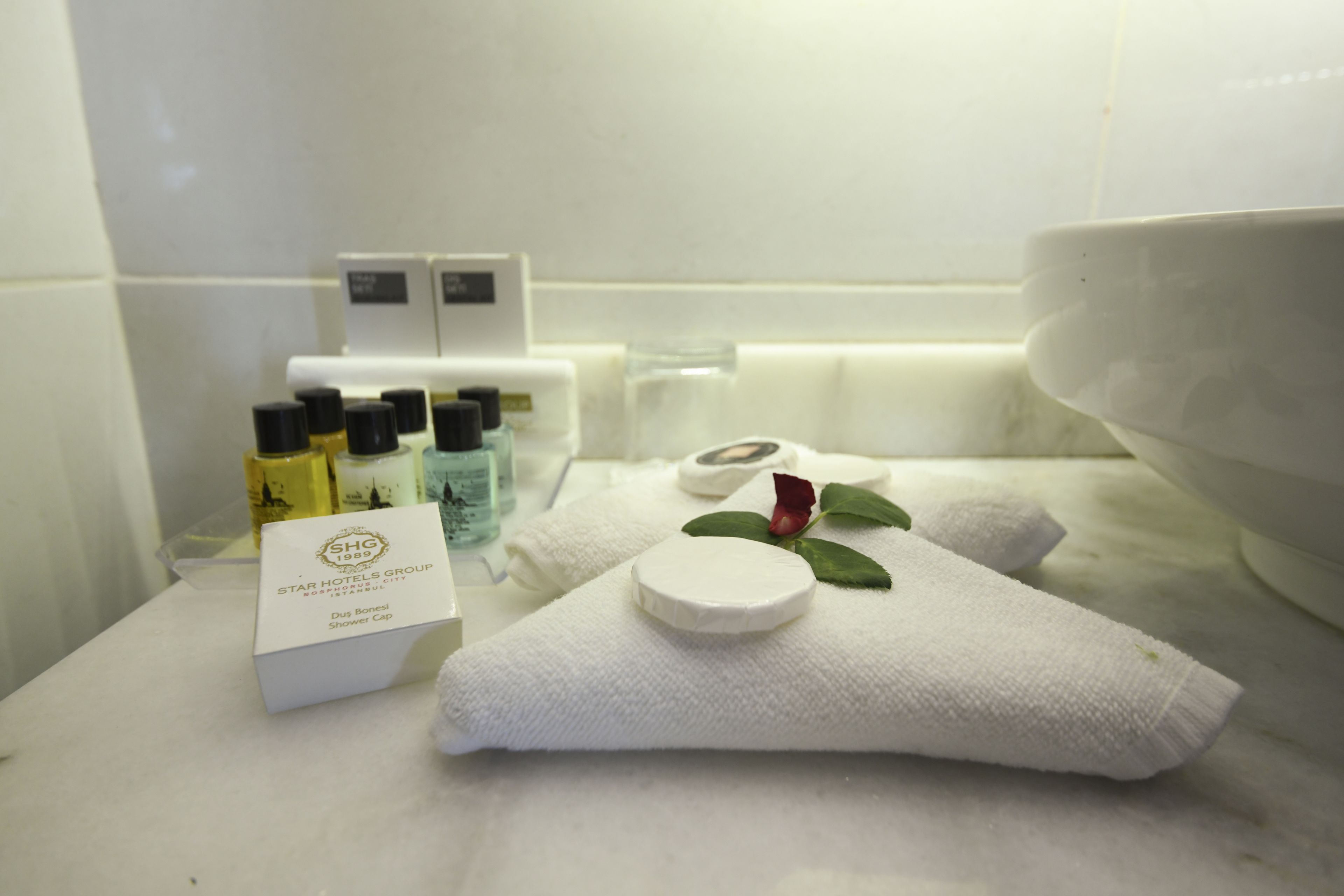 A bathroom with toiletries, a shower cap, and a towel with a rose.