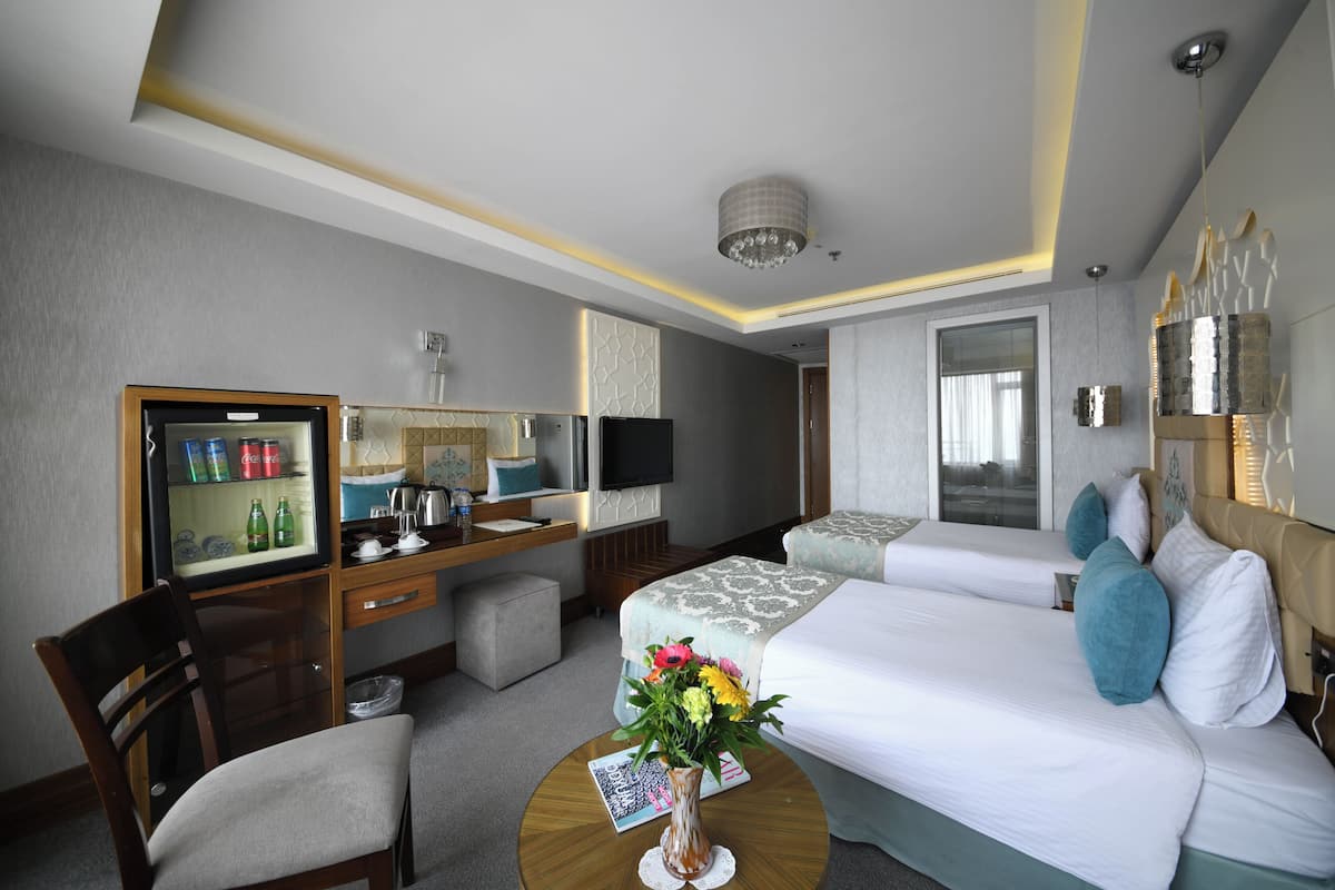 A hotel room with a bed, a desk with a computer, a chair, a coffee table with a magazine and a vase of flowers.