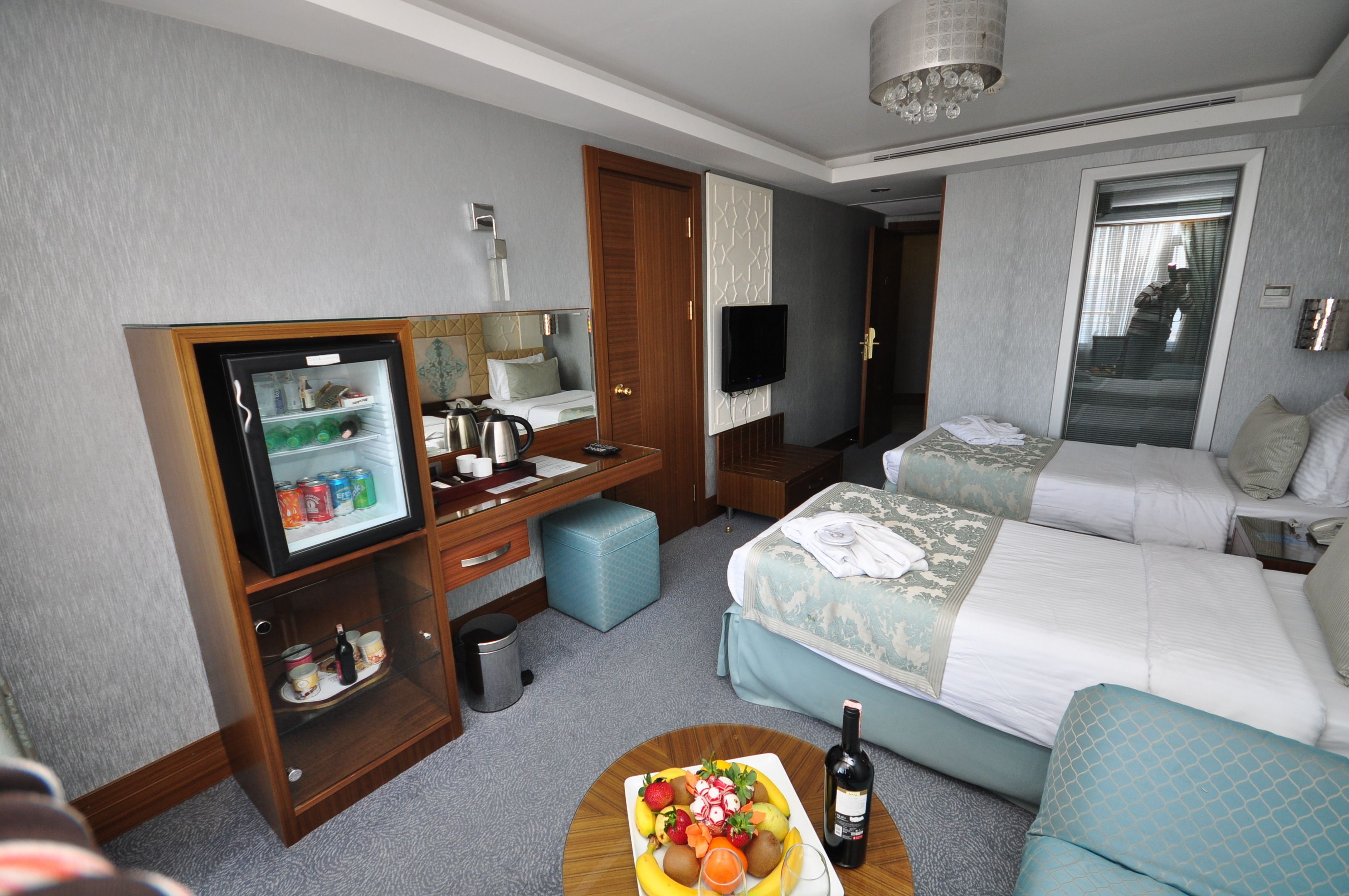 A hotel room with a bed, a desk with a computer, a television, a minibar, and a breakfast tray.