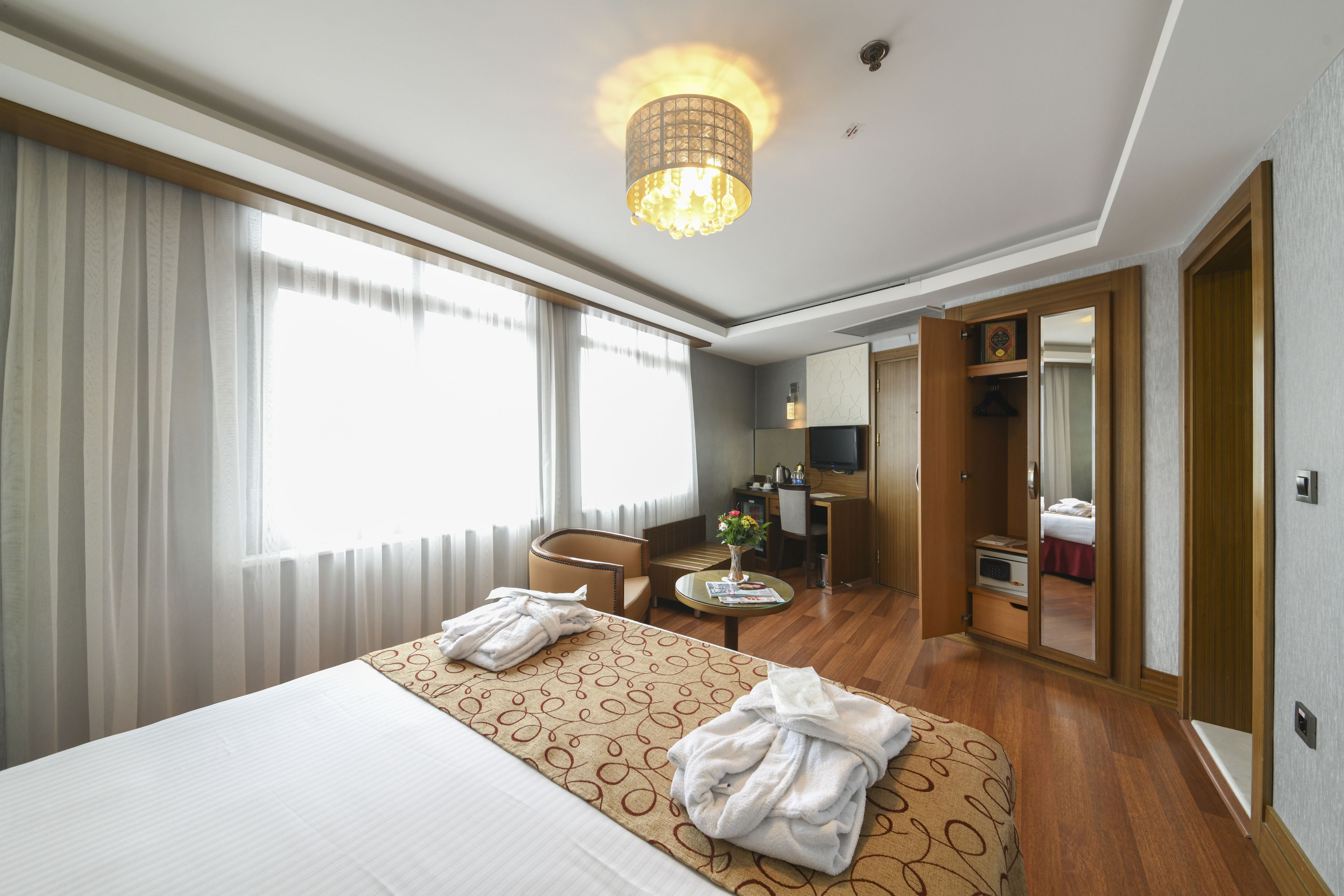 Une chambre d’hôtel dotée d’un grand lit, d’un coin salon avec une table et des chaises, d’une petite kitchenette et d’une salle de bain visible à travers une porte ouverte.