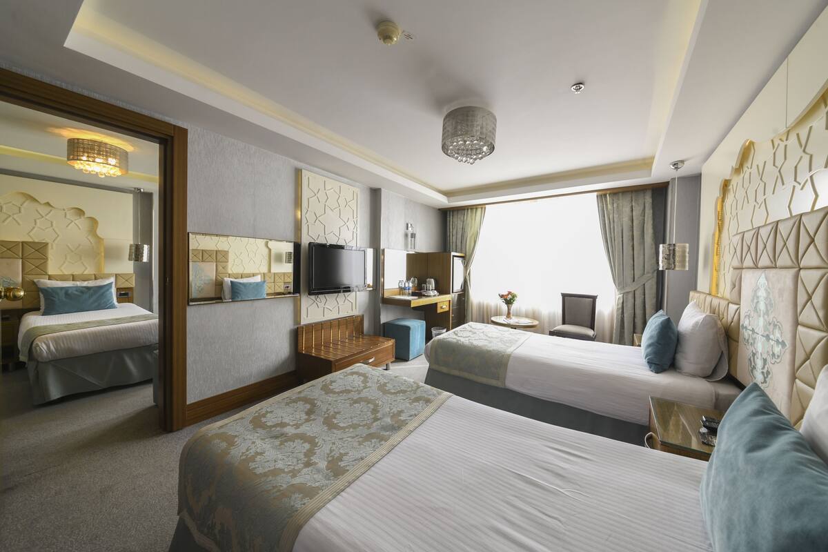 A hotel room with two beds, a desk, a TV, and a chandelier.