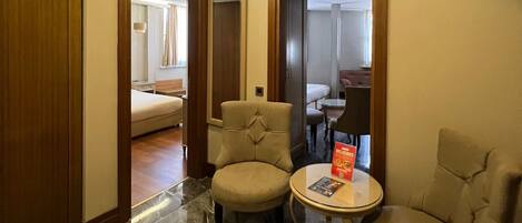 Ein Hotelzimmer mit Marmorboden, zwei Sesseln, einem kleinen Tisch mit einer Zeitschrift und einem Bett im Hintergrund.