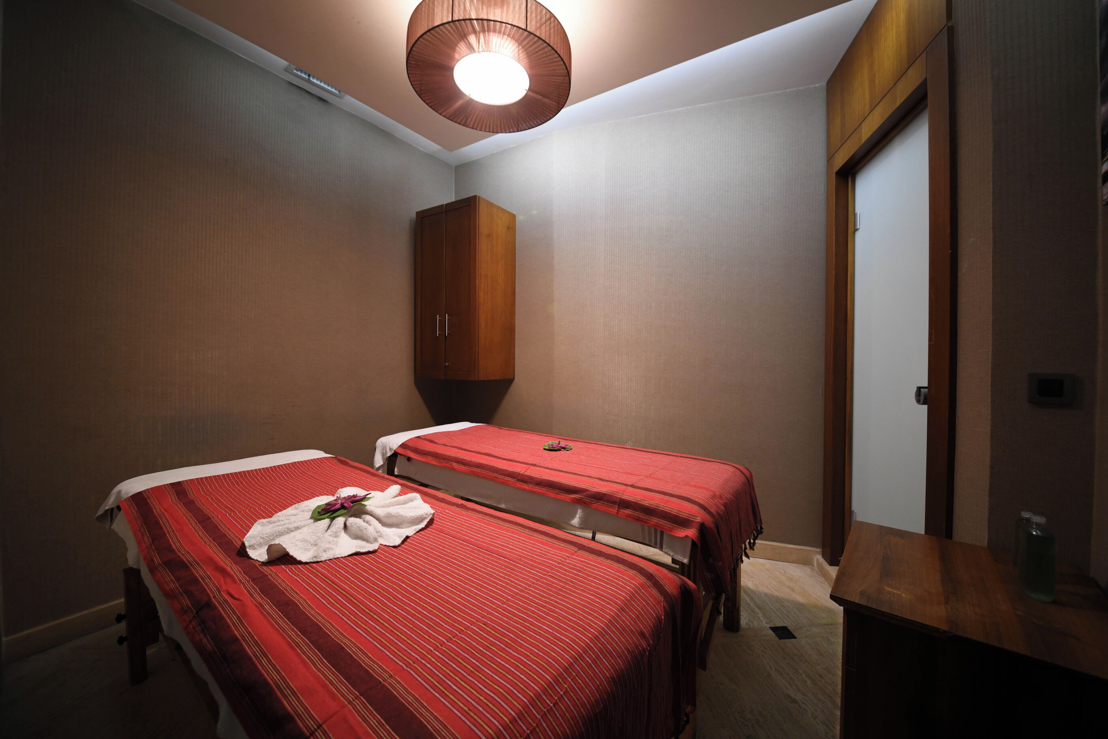 A hotel room with two single beds, a wooden wardrobe, a small table, and a door.