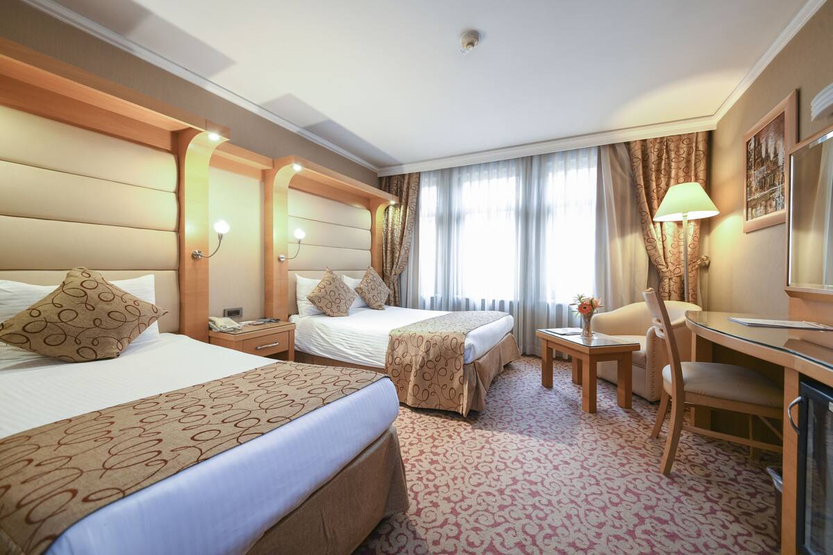 A hotel room with two beds, a desk, a chair, and a small table.