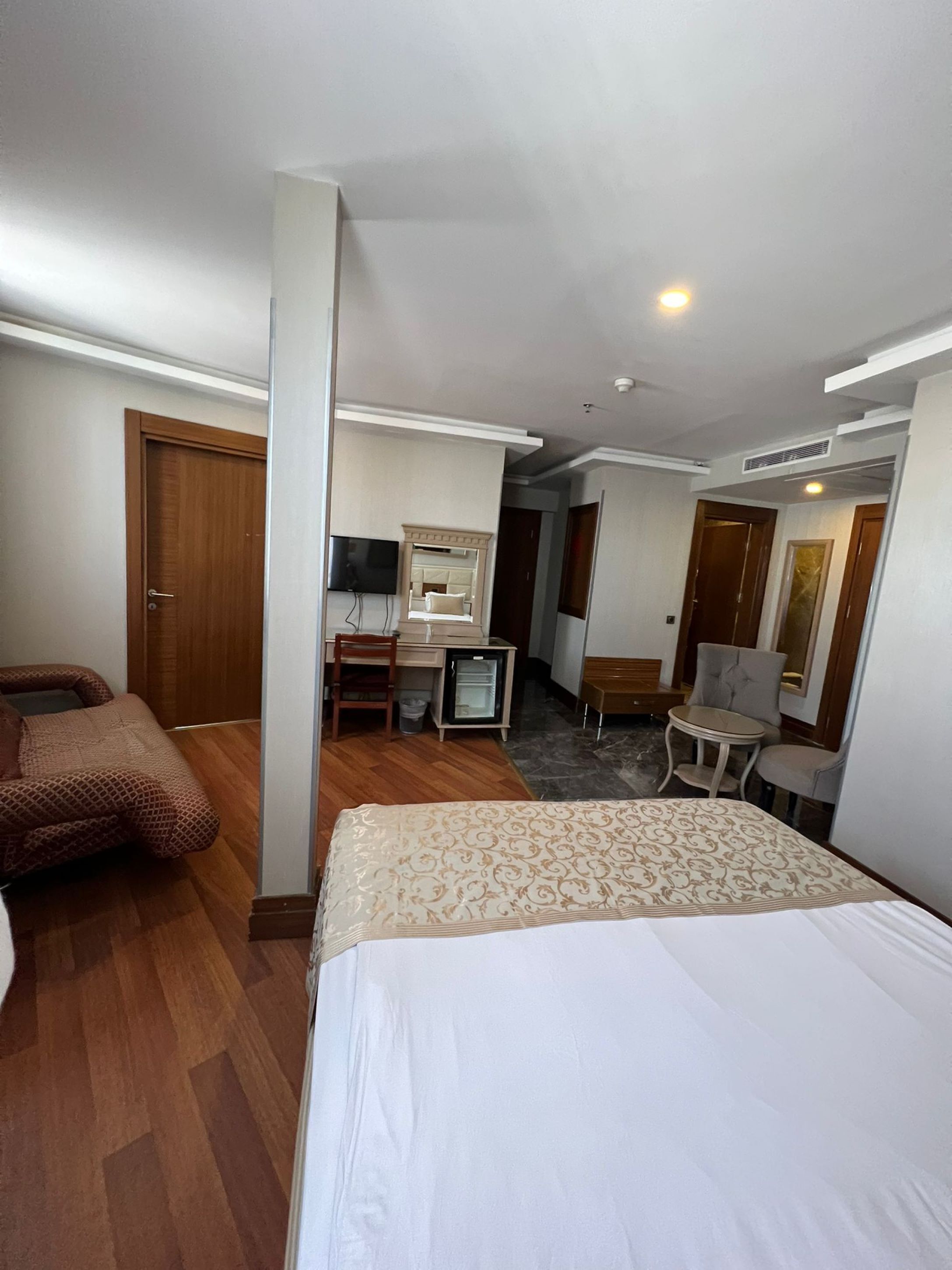 A hotel room with a bed, a desk with a chair, a television, and a small table with two chairs.