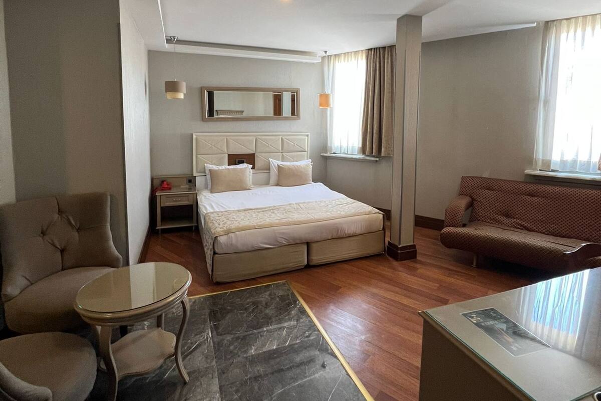 A hotel room with a bed, a sofa, a small table, a mirror, and a ceiling fan.