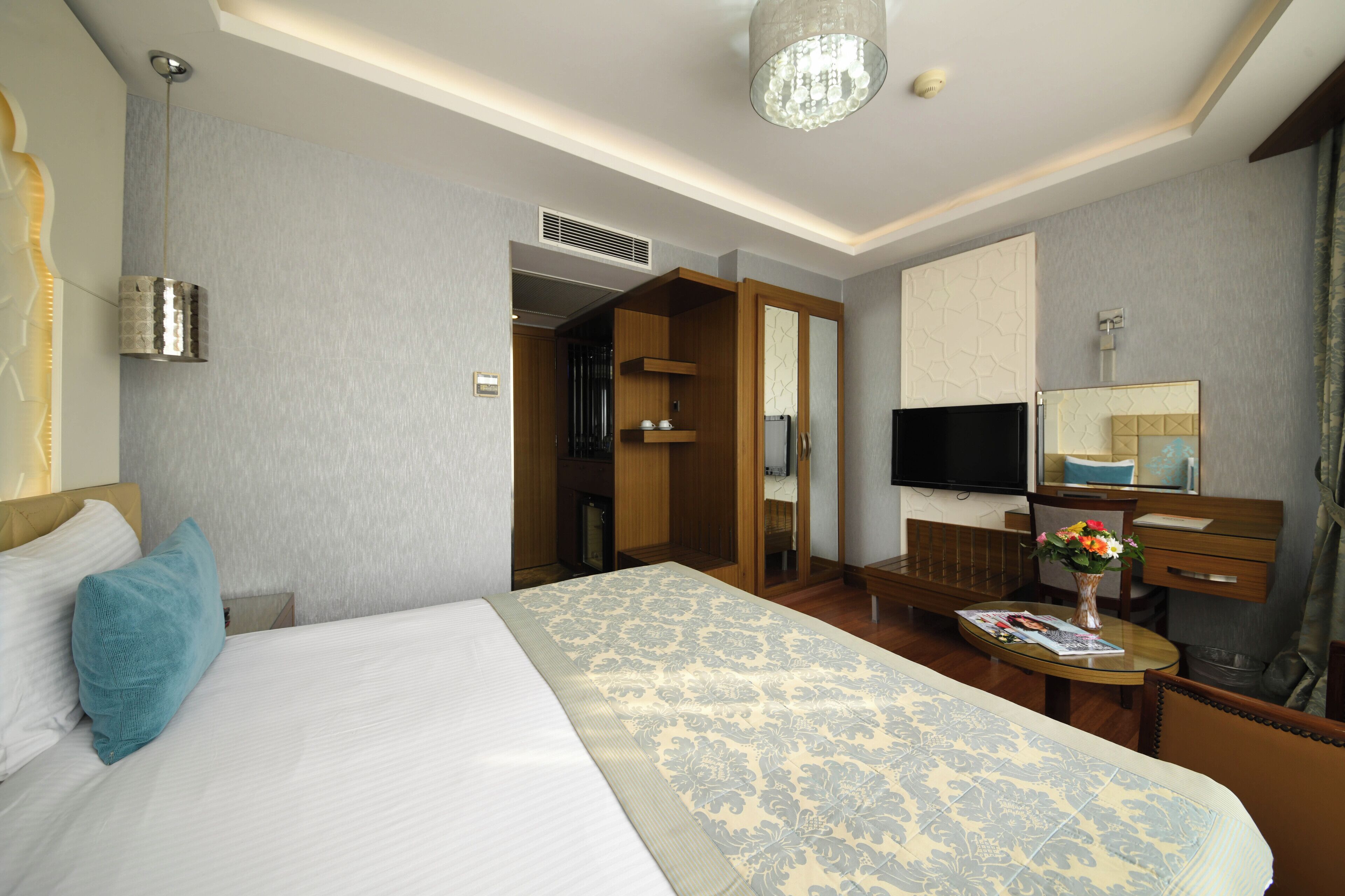 Habitación de hotel con cama, escritorio, silla, televisor y baño visible a través de una puerta abierta.
