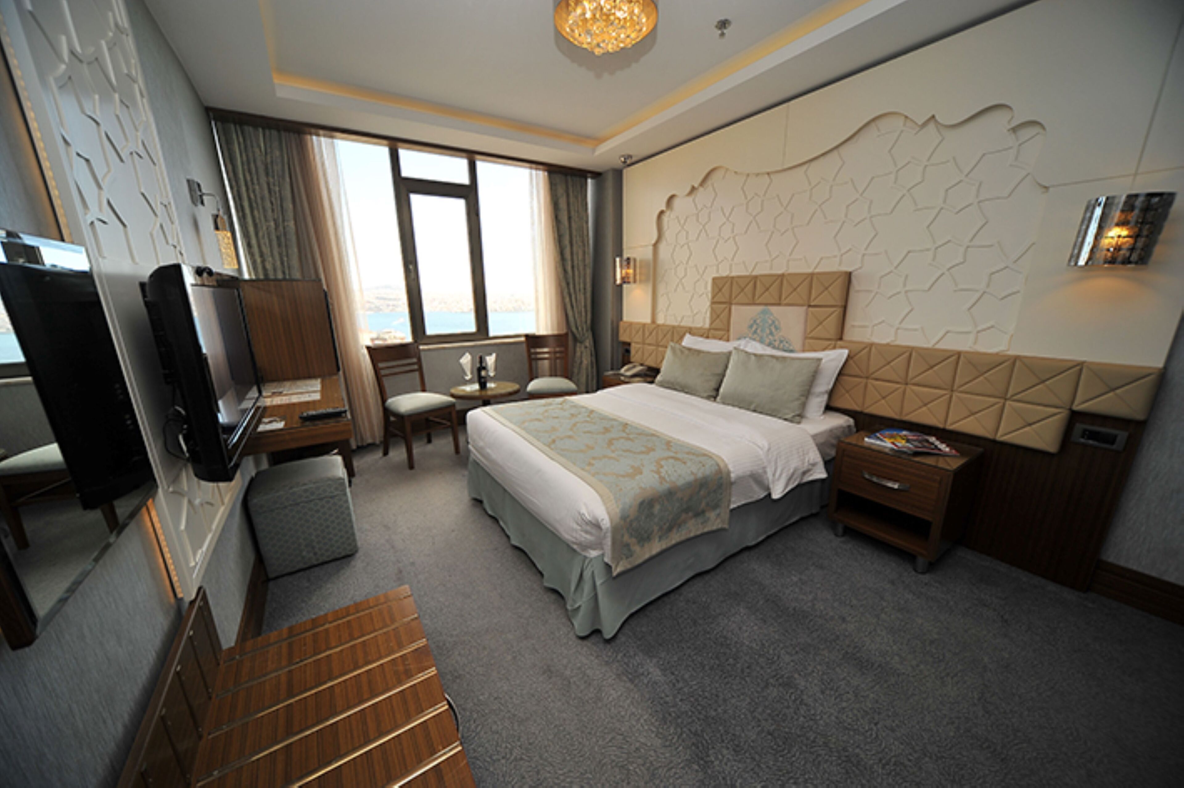Une chambre d’hôtel avec un grand lit, un bureau avec une chaise, une télévision et une vue sur la mer par la fenêtre.