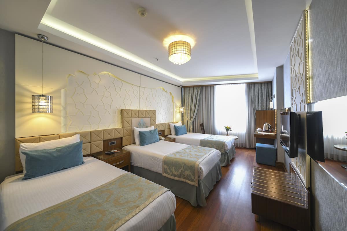 A hotel room with three beds, a TV, a desk, and a bathroom.