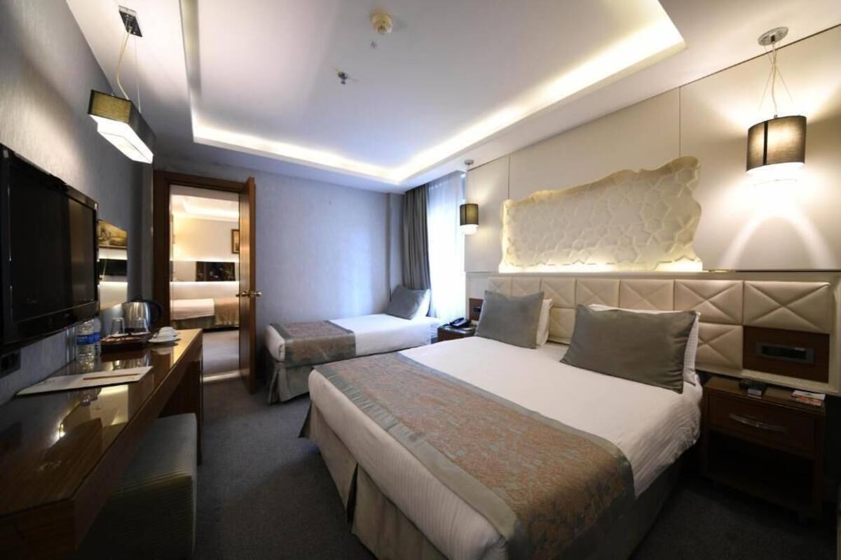 A hotel room with two beds, a desk with a chair, a TV, and a large decorative wall piece.