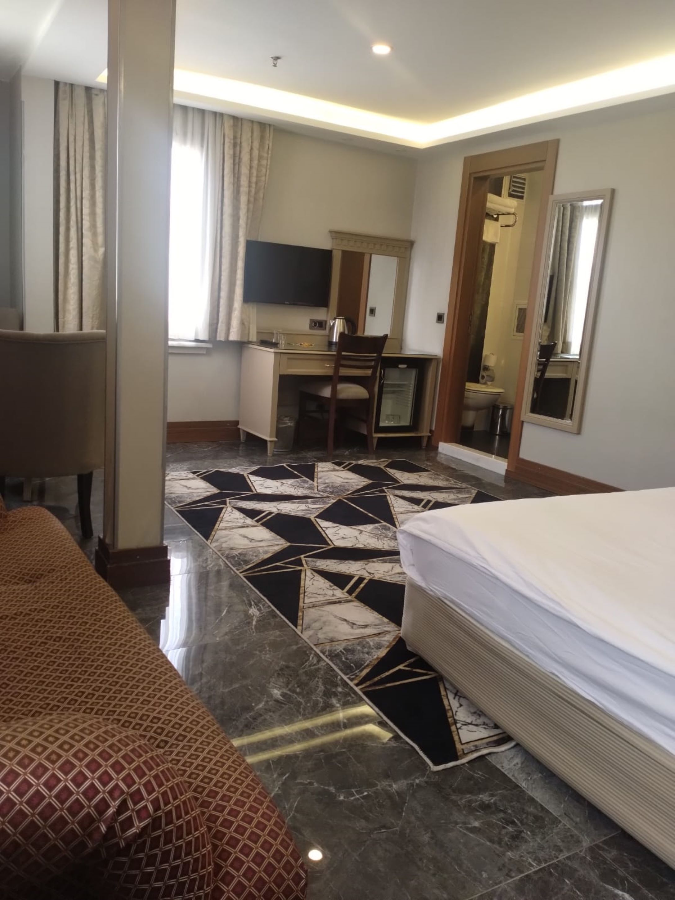 Habitación de hotel con cama, escritorio, silla, televisor y espejo de baño.