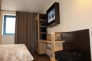 A hotel room with a bed, a TV mounted on a wooden shelf, a desk, and a suitcase on the floor. - Eurohotel Airport Orly Rungis (Fresnes)