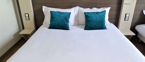 Una habitación de hotel con una cama grande, dos almohadas color turquesa, ropa de cama blanca y lámparas de noche.