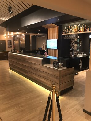 A modern bar area with a long counter, a television screen, and a variety of bottles on shelves. - Eurohotel Airport Orly Rungis (Fresnes)