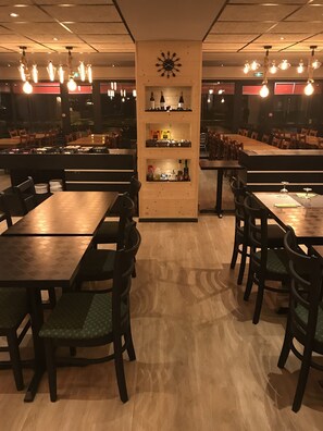 A restaurant interior with wooden tables and chairs, a central decorative wall with a clock, and hanging light fixtures. - Eurohotel Airport Orly Rungis (Fresnes)