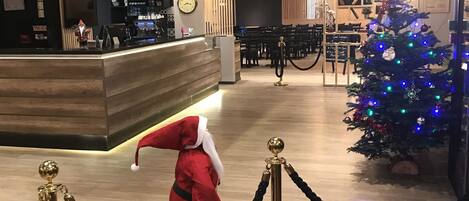 Un vestíbulo de hotel con una recepción, un árbol de Navidad y una estatua de Papá Noel.