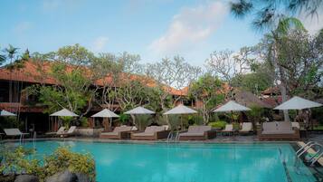 A pool area with lounge chairs and umbrellas, surrounded by trees and buildings with red roofs.