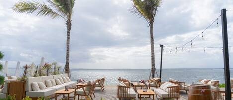 An outdoor seating area with a view of the sea, featuring a sofa, chairs, and tables.