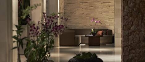 A modern living room with a sofa and coffee table, a brick wall, and potted plants.