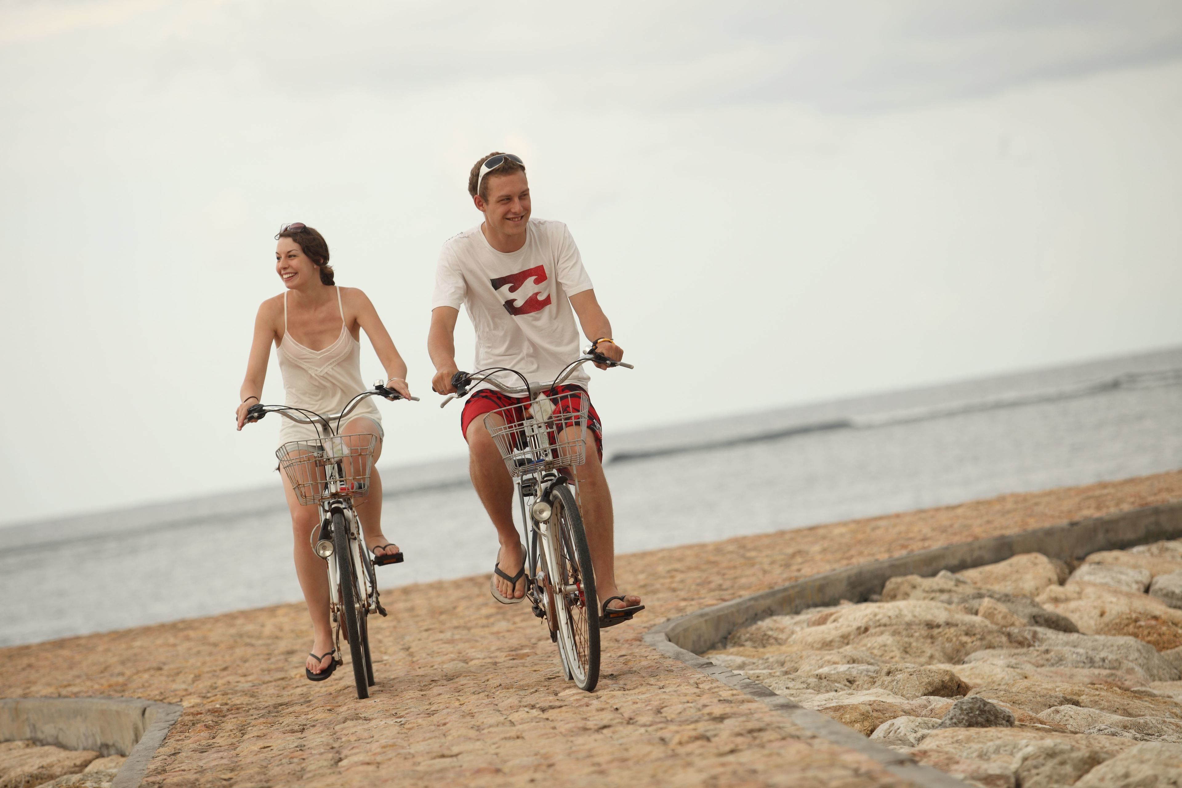 Two people riding bicycles on a rocky beach with the ocean in the background.