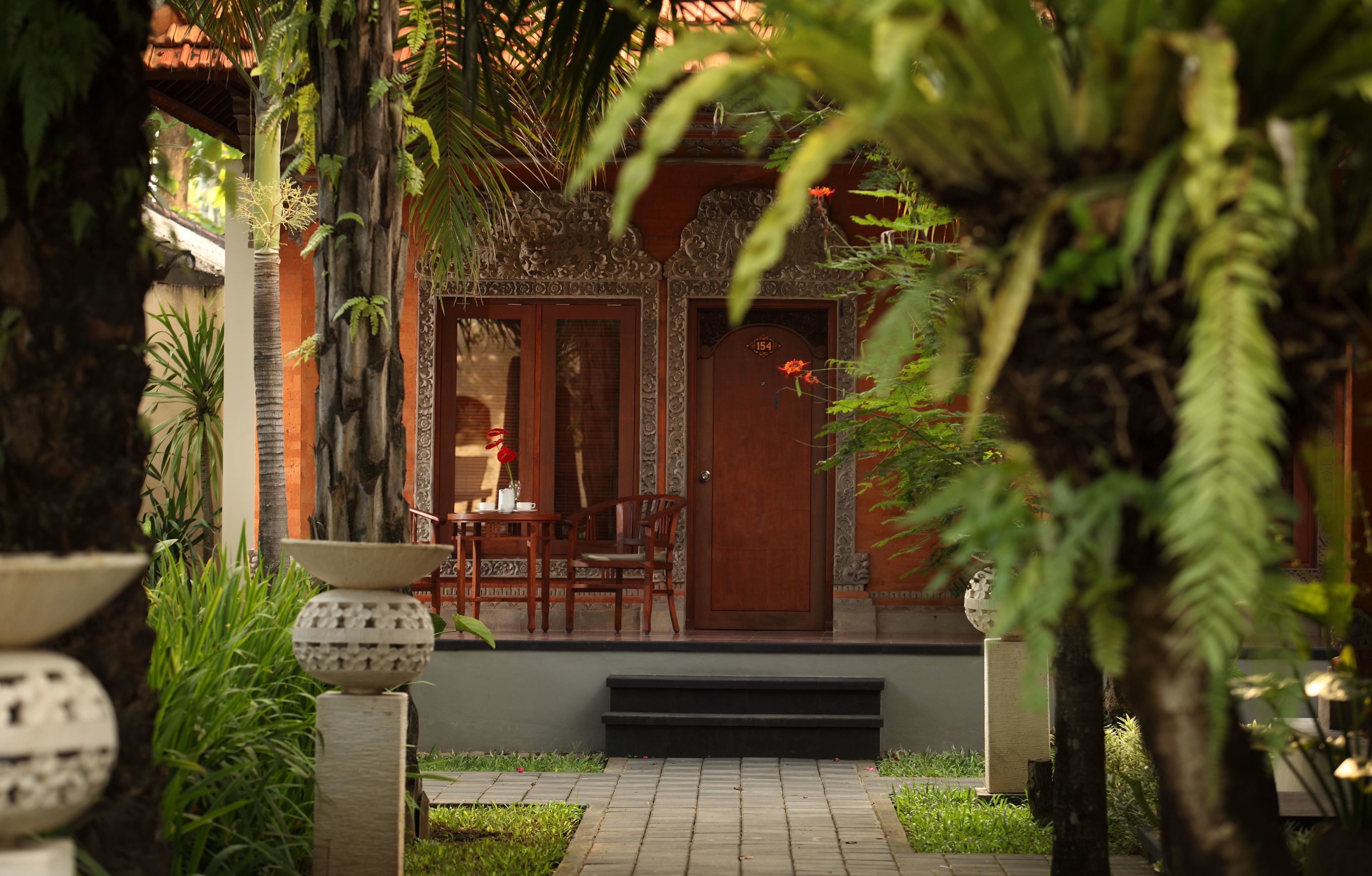 A traditional wooden building with a tiled entrance, surrounded by lush greenery and a small outdoor seating area with chairs and a table.