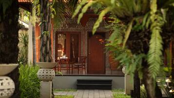 A traditional wooden building with a tiled entrance, surrounded by lush greenery and a small outdoor seating area with chairs and a table.
