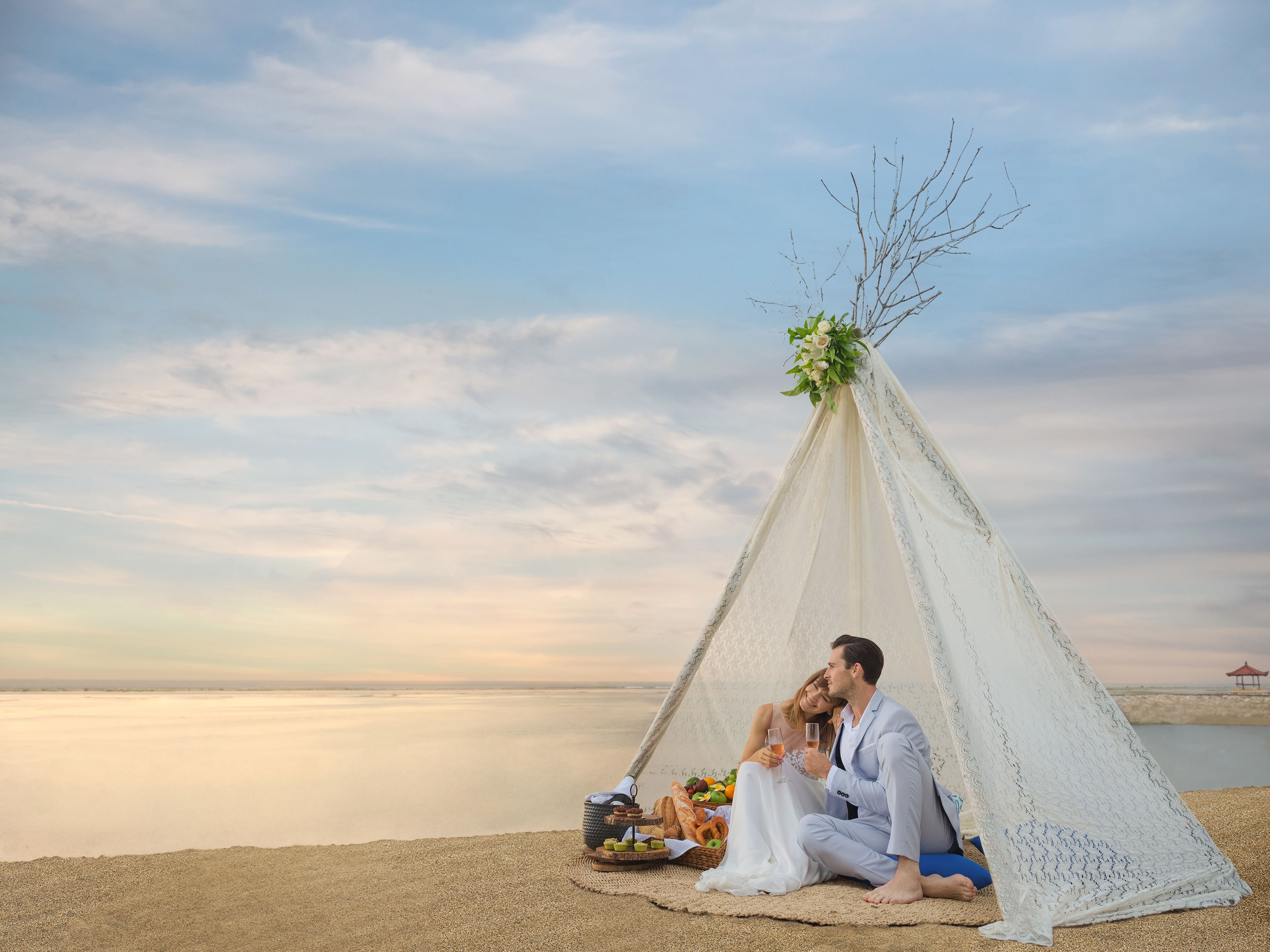 A couple in a white tent with a view of a calm body of water.