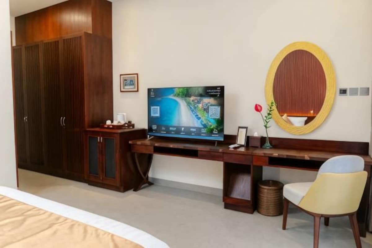 A hotel room with a bed, a wooden desk with a television, a mirror, and a chair.