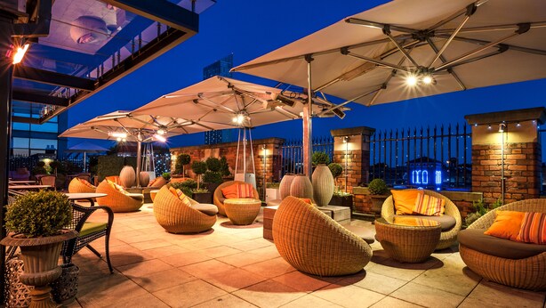 An outdoor patio area with wicker furniture, umbrellas, and a brick wall. - Great John Street Hotel (Manchester)
