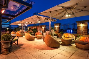 An outdoor patio area with wicker furniture, umbrellas, and a brick wall. - Great John Street Hotel (Manchester)