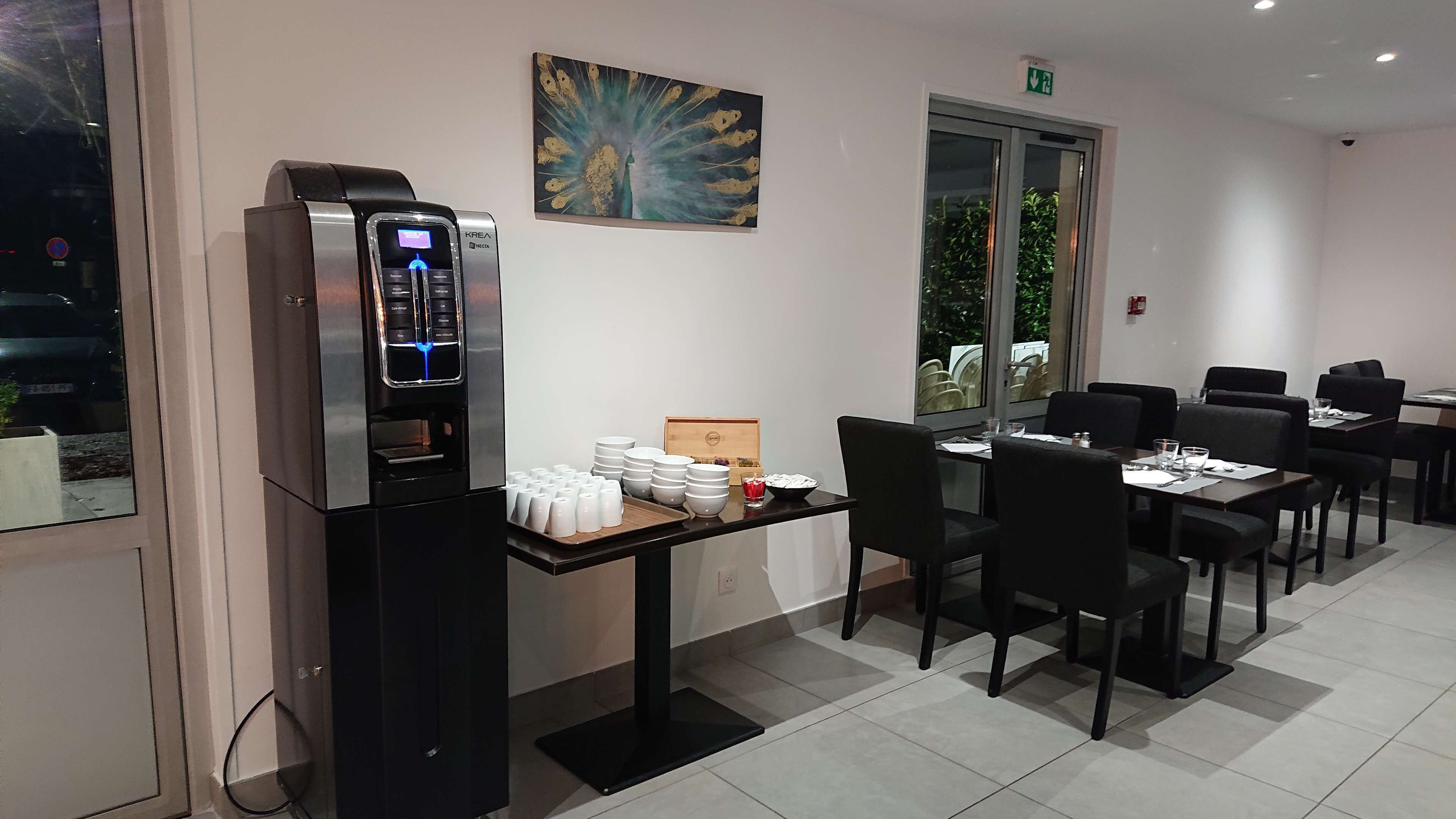 Un comedor con una cafetera, mesas, sillas y un cuadro decorativo.
