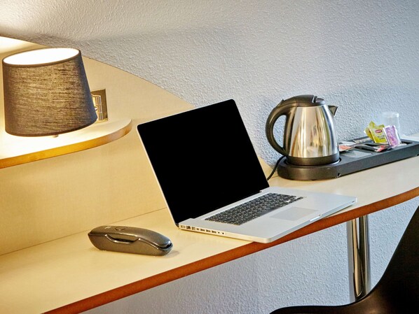 A laptop on a desk with a mouse, a lamp, and a coffee pot.