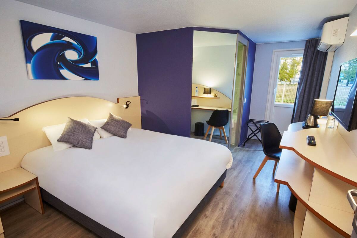 Quarto de hotel com uma cama grande, uma escrivaninha, uma cadeira e um computador.