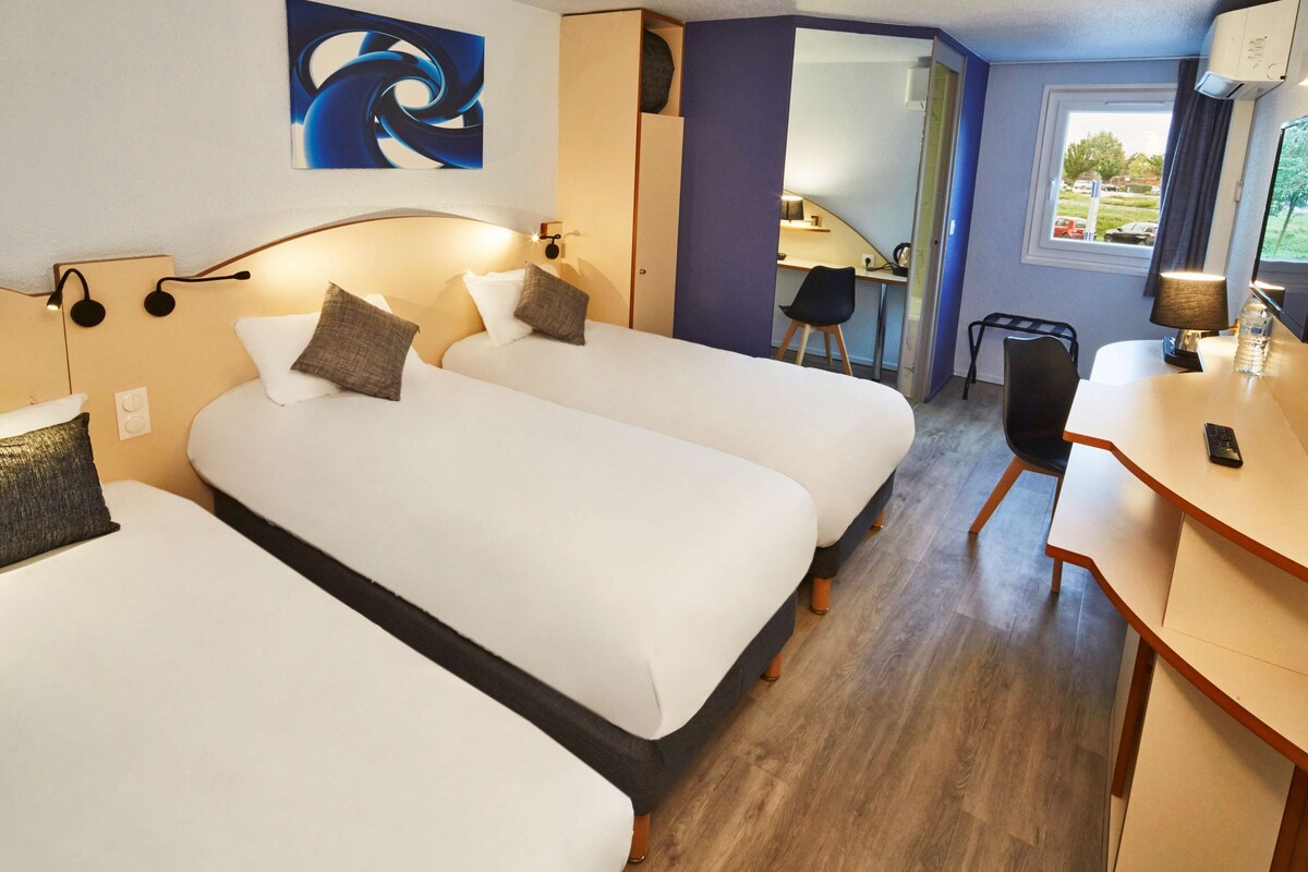 A hotel room with two beds, a desk, a chair, a lamp, and a painting on the wall.